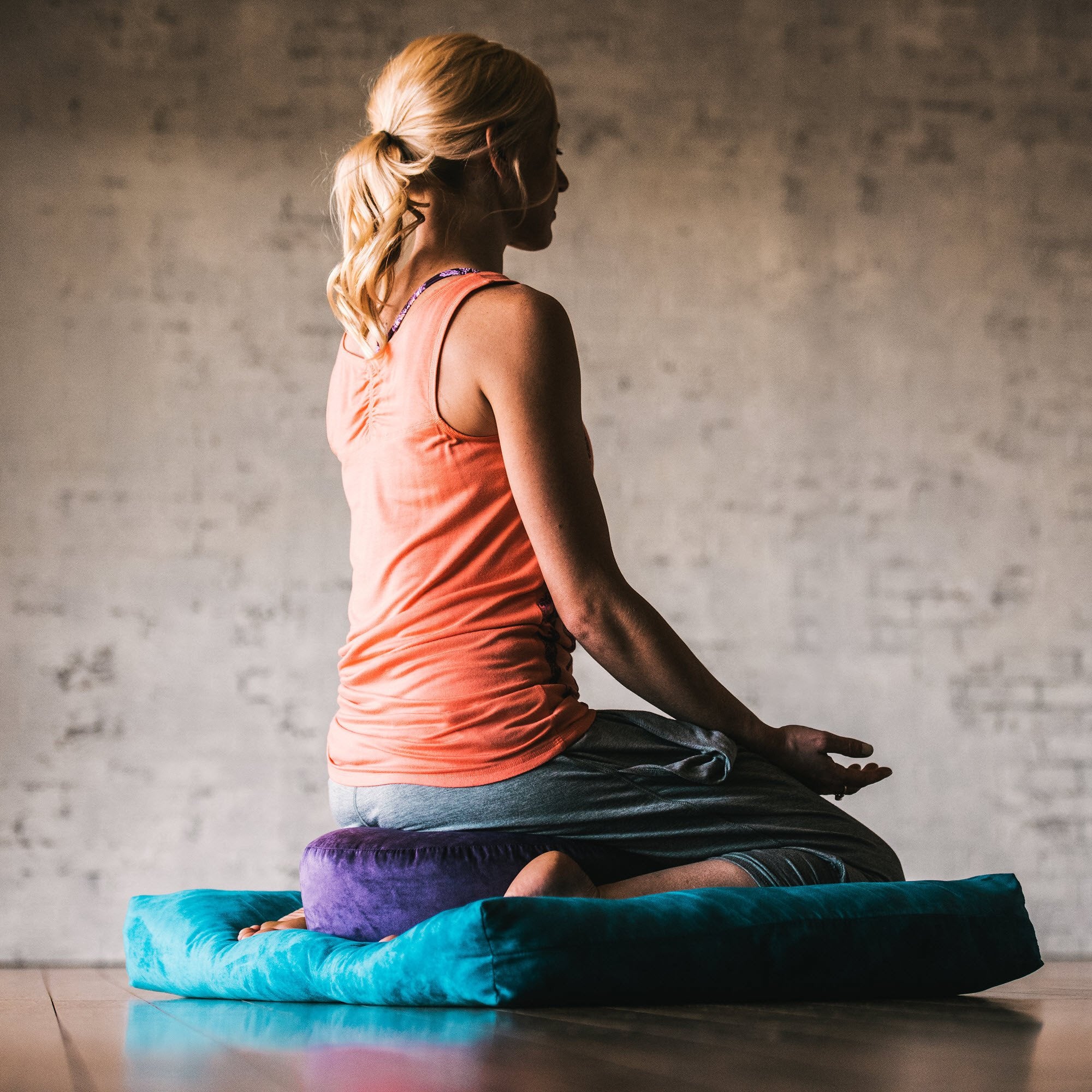 Woman meditating on the purple zafu cushion stacked on top of the blue zabuton floor cushion